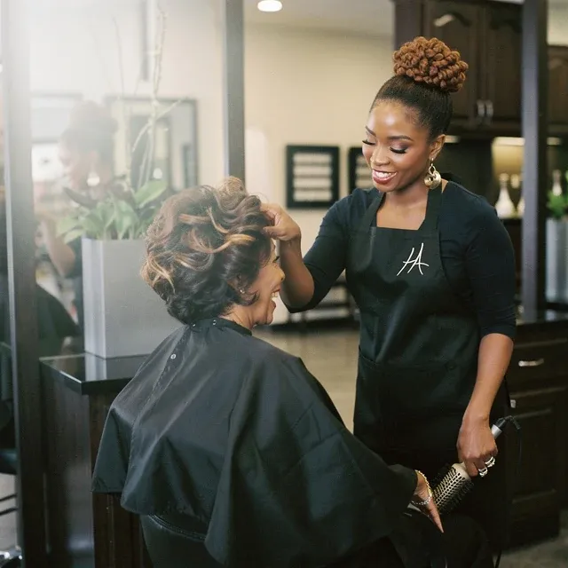 A student blow-drying and shaping a guest's hair at the styling station