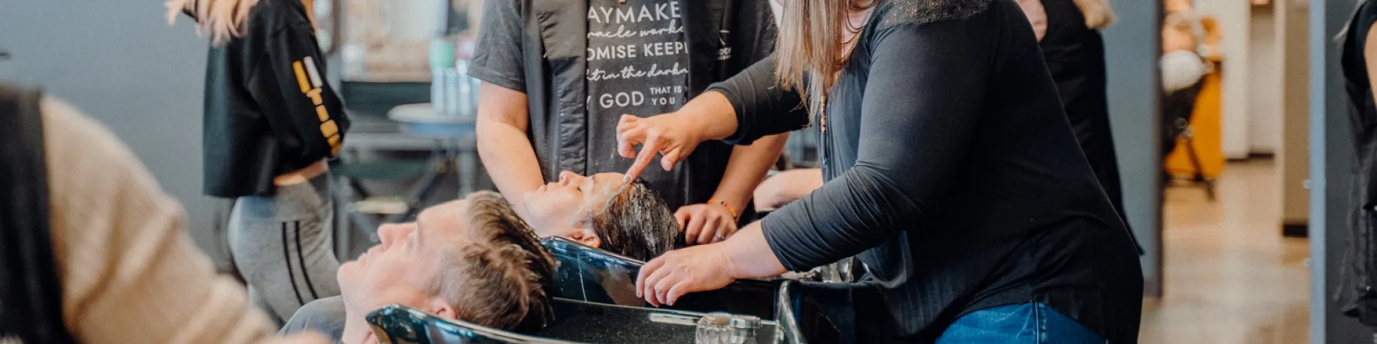 Students working with clients at the shampoo bowls on the Hays salon floor